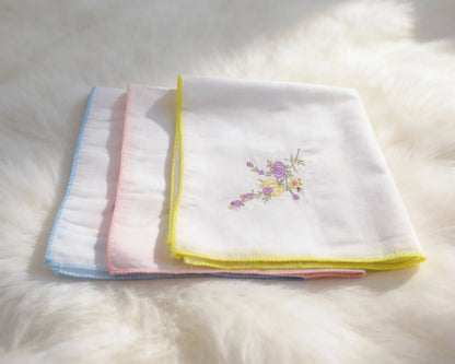 Set of folded white towels with colorful embroidery on a fluffy white surface
