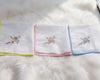 Set of folded white towels with colorful embroidery on a fluffy white surface
