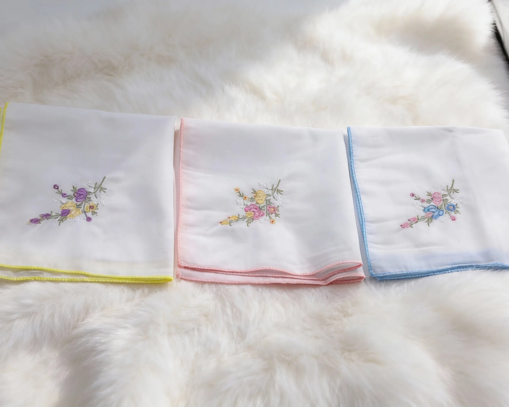 Set of folded white towels with colorful embroidery on a fluffy white surface