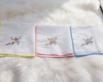 Set of folded white towels with colorful embroidery on a fluffy white surface