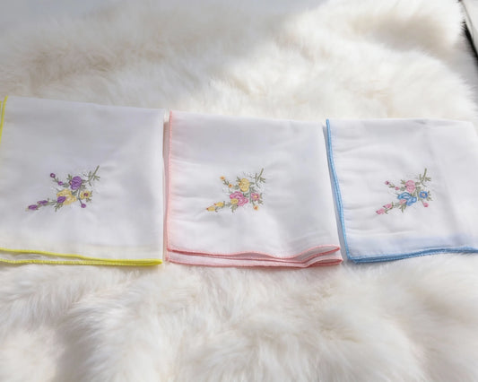Set of folded white towels with colorful embroidery on a fluffy white surface